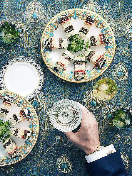 Draufsicht auf einen Tisch im Retro-Stil mit Sandwiches aus Schichtband und einem Weinglas in der Hand