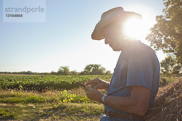 Landwirt mit Handy bei Heuballen