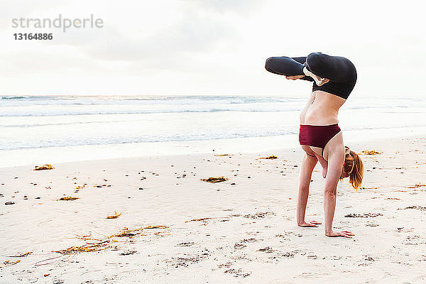 Mittelgroße erwachsene Frau kopfüber in Yogastellung am Strand