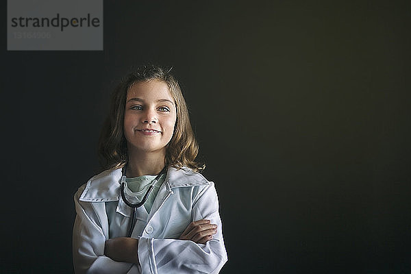 Porträt eines als Arzt verkleideten Mädchens mit Stethoskop  die Arme verschränkt und lächelnd wegschauend