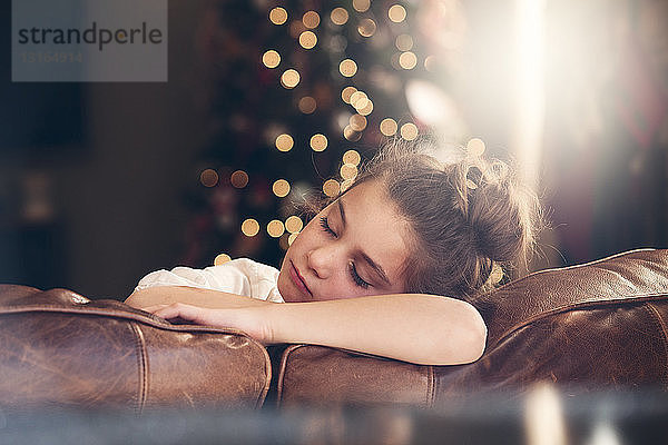 Porträt eines auf dem Sofa schlafenden Mädchens vor dem Weihnachtsbaum