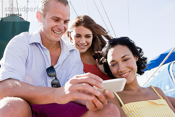 Drei junge Freunde auf einer Yacht mit Smartphone