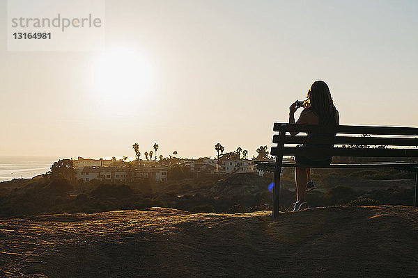 Silhouette einer jungen Frau  die auf einer Klippenbank sitzt und die Ansicht auf einem Smartphone fotografiert  San Clemente  Kalifornien  USA