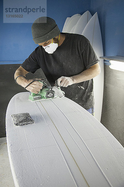 Mittlerer erwachsener männlicher Surfer beim Schleifen von Surfbrettern in einem Workshop