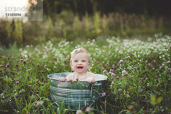 Kleines Mädchen badet in einer Blechbadewanne auf einer Wildblumenwiese