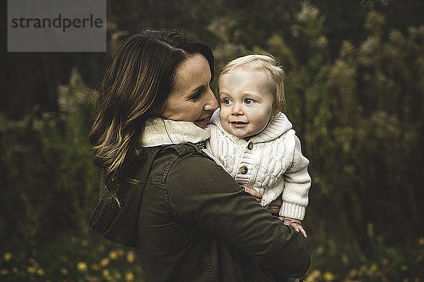 Taillenaufwärts-Seitenansicht einer Mutter  die im Herbst ein Baby hält