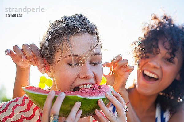 Junge Frau isst Wassermelone  während ihr Freund an den Ohren zieht