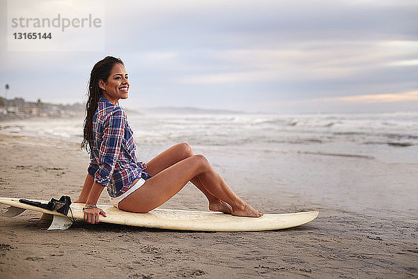 Junge Frau sitzt am Strand auf einem Surfbrett  San Diego  Kalifornien  USA