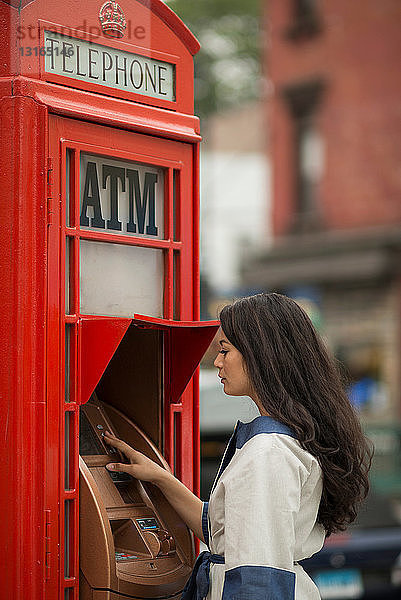 Mittelgroße erwachsene Frauen  die einen Geldautomaten in einer öffentlichen Telefonzelle benutzen