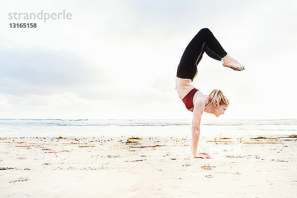 Mittlere erwachsene Frau  die am Strand Yoga im Handstand praktiziert