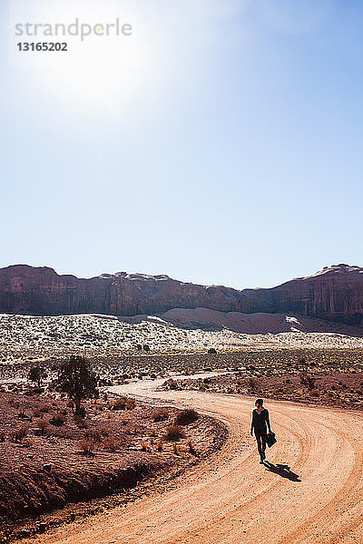 Mittelgroße erwachsene Frau  die entlang einer ländlichen Schotterstraße geht  Monument Valley  Utah  USA