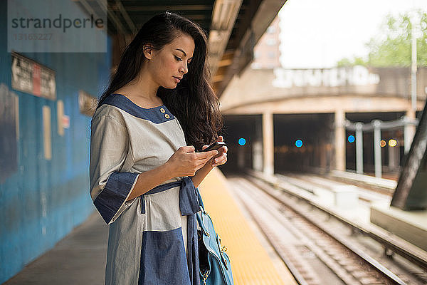 Mittelgroße erwachsene Frauen  die ein Mobiltelefon auf dem U-Bahn-Bahnsteig benutzen  Brooklyn  New York