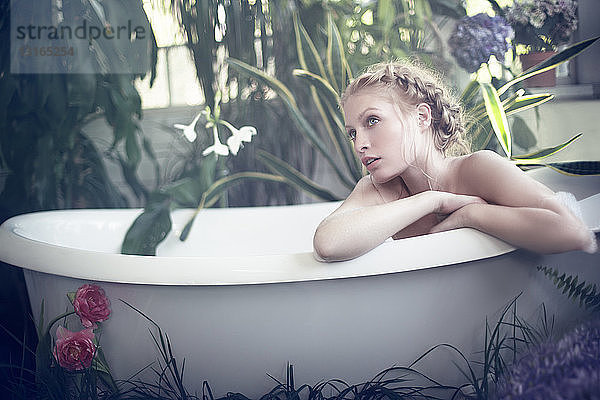 Nackte junge Frau entspannt sich in der Badewanne  im Badezimmer voller Pflanzen