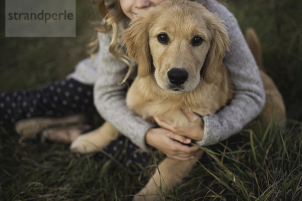 Junges Mädchen sitzt im Gras und umarmt seinen Hund