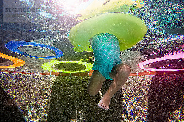 Unterwasseraufnahme eines Mädchens  das im Schwimmbad mit einem Gummiring gegen die Beine tritt und schwimmen lernt