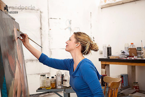 Mittlere erwachsene Frau malt auf Leinwand im Künstleratelier