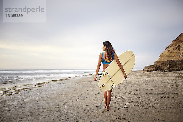Rückansicht einer jungen Frau  die mit einem Surfbrett am Strand spazieren geht  San Diego  Kalifornien  USA
