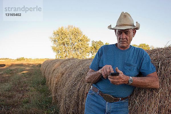 Landwirt mit Handy bei Heuballen