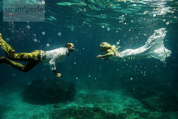 Paar in Hochzeitskleidung  unter Wasser  aufeinander zu schwimmen