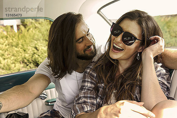 Junges lachendes Paar auf dem Rücksitz eines Autos