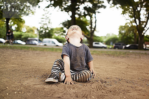 Männliches Kleinkind sitzt im Park und schaut auf