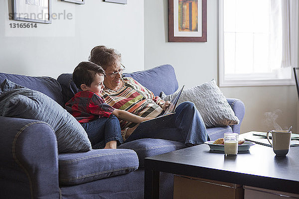Ältere Frau liest Buch mit Enkel auf Sofa