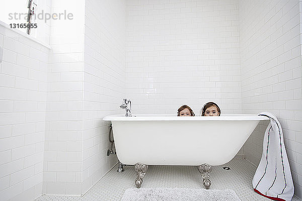 Porträt von zwei jungen Mädchen  die über der Badewanne spähen