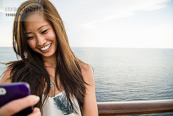 Junge Frau benutzt Mobiltelefon auf See