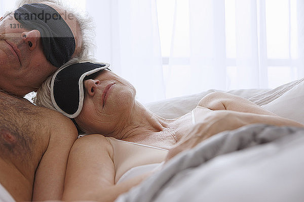 Älteres Ehepaar schläft mit Gesichtsmasken im Bett