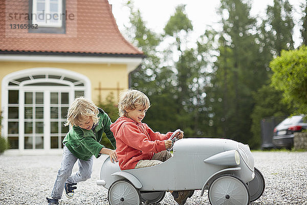 Zwei Jungen spielen mit einem Oldtimer-Spielzeugauto vor dem Haus
