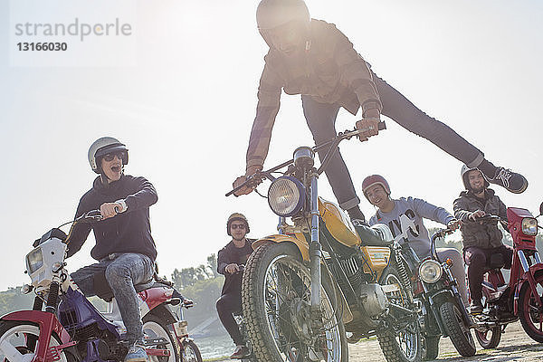 Eine Gruppe von Freunden fährt mit Mopeds die Straße entlang  ein Mann in der Luft  macht einen Stunt