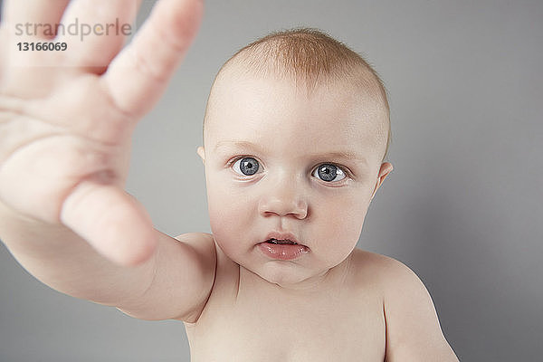 Studioporträt eines kleinen Jungen mit erhobener Hand