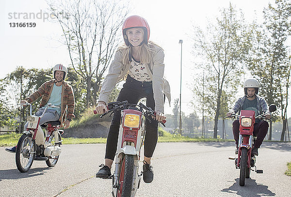 Eine Gruppe von Freunden fährt mit Mopeds entlang der Straße  im Vordergrund eine junge Fahrerin