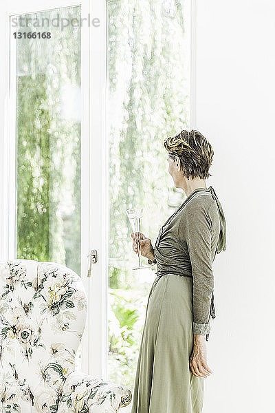 Porträt einer älteren Frau  die im Wohnzimmer aus dem Fenster schaut