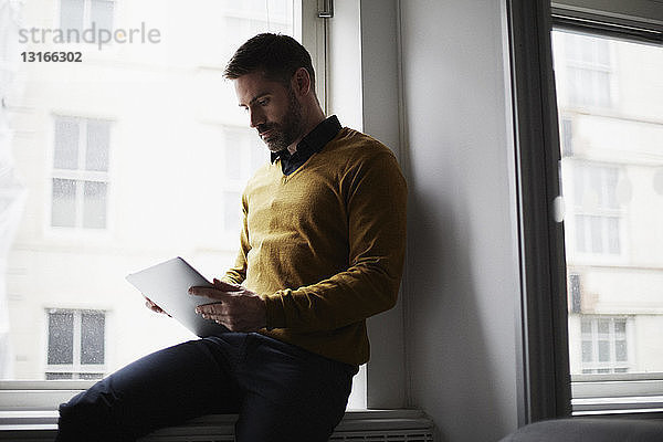 Gelegenheits-Geschäftsmann sitzt auf der Fensterbank mit digitalem Tablett
