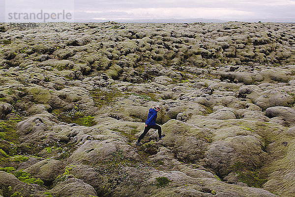 Seitenansicht einer mittleren erwachsenen Frau  die über eine hügelige Vulkanlandschaft läuft  Island