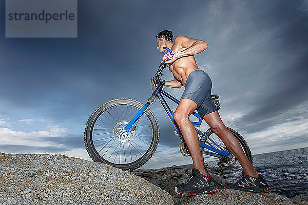 Mann schiebt Fahrrad auf Felsbrocken