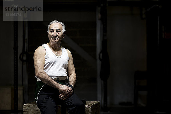 Porträt eines grauhaarigen älteren Mannes  der in dunkler Turnhalle sitzt