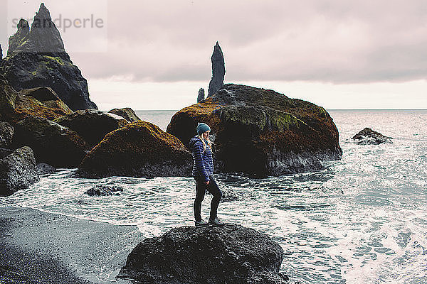 Seitenansicht einer mittleren erwachsenen Frau  die auf einem Felsen an der Küste steht und auf den Ozean schaut  Island