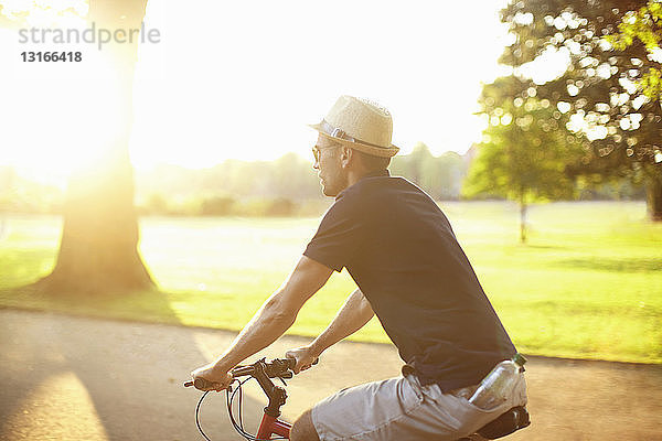 Mittelgroßer erwachsener Mann fährt Fahrrad im sonnenbeschienenen Park