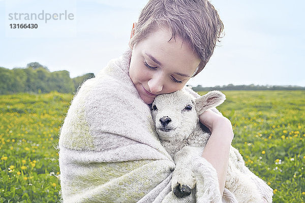 Bildnis einer jungen Frau im Feld  die ein Lamm trägt und in eine Decke gehüllt ist