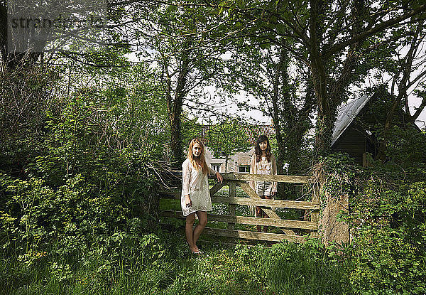 Porträt von zwei jungen Frauen  die vom Feldtor aus starr in die Landschaft blicken