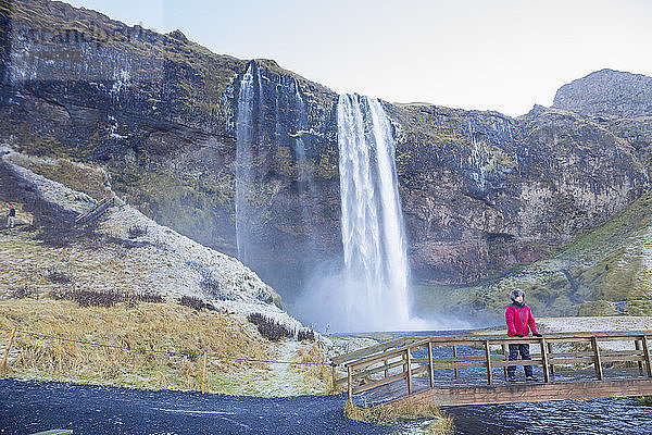 Frau auf der Brücke stehend  Blick auf den Seljalandsfoss-Wasserfall hinter ihr  Südwest-Island