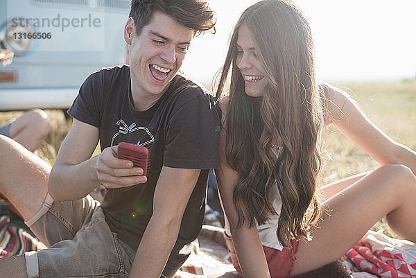 Junges Paar sitzt mit Smartphone im Freien