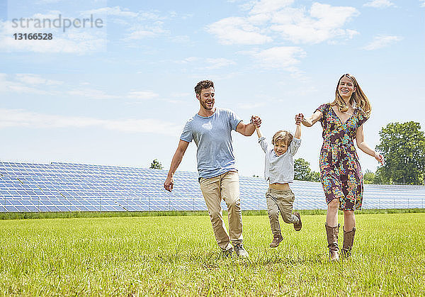 Mutter und Vater halten mit dem Sohn Händchen und gehen über das Feld neben dem Solarpark