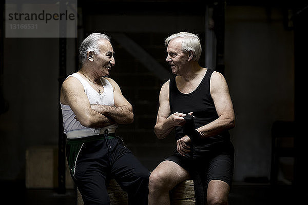 Zwei ältere Männer unterhalten sich und bereiten sich in dunkler Turnhalle vor