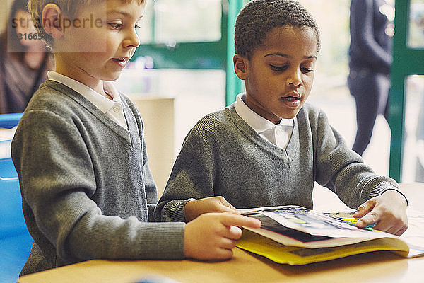 Zwei Jungen lesen ein Märchenbuch am Schreibtisch im Klassenzimmer der Grundschule