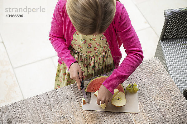 Hochwinkelansicht eines Mädchens am Küchentisch  das frisches Obst schneidet