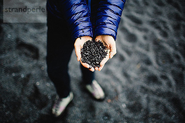 Hände einer mittleren erwachsenen Frau  die schwarzen Sand hält  Draufsicht  Island