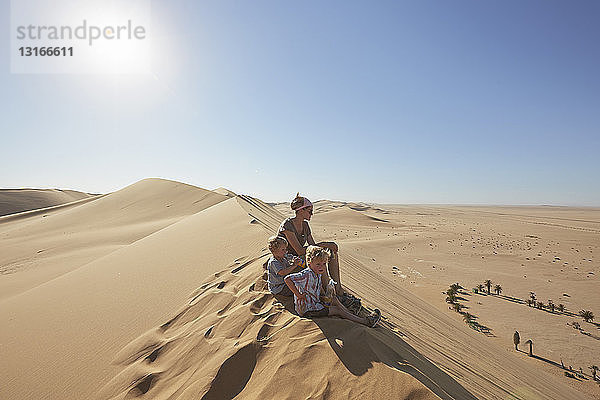 Mutter und Söhne sitzen auf einer Sanddüne  Düne 7  Namib-Naukluft-Nationalpark  Afrika